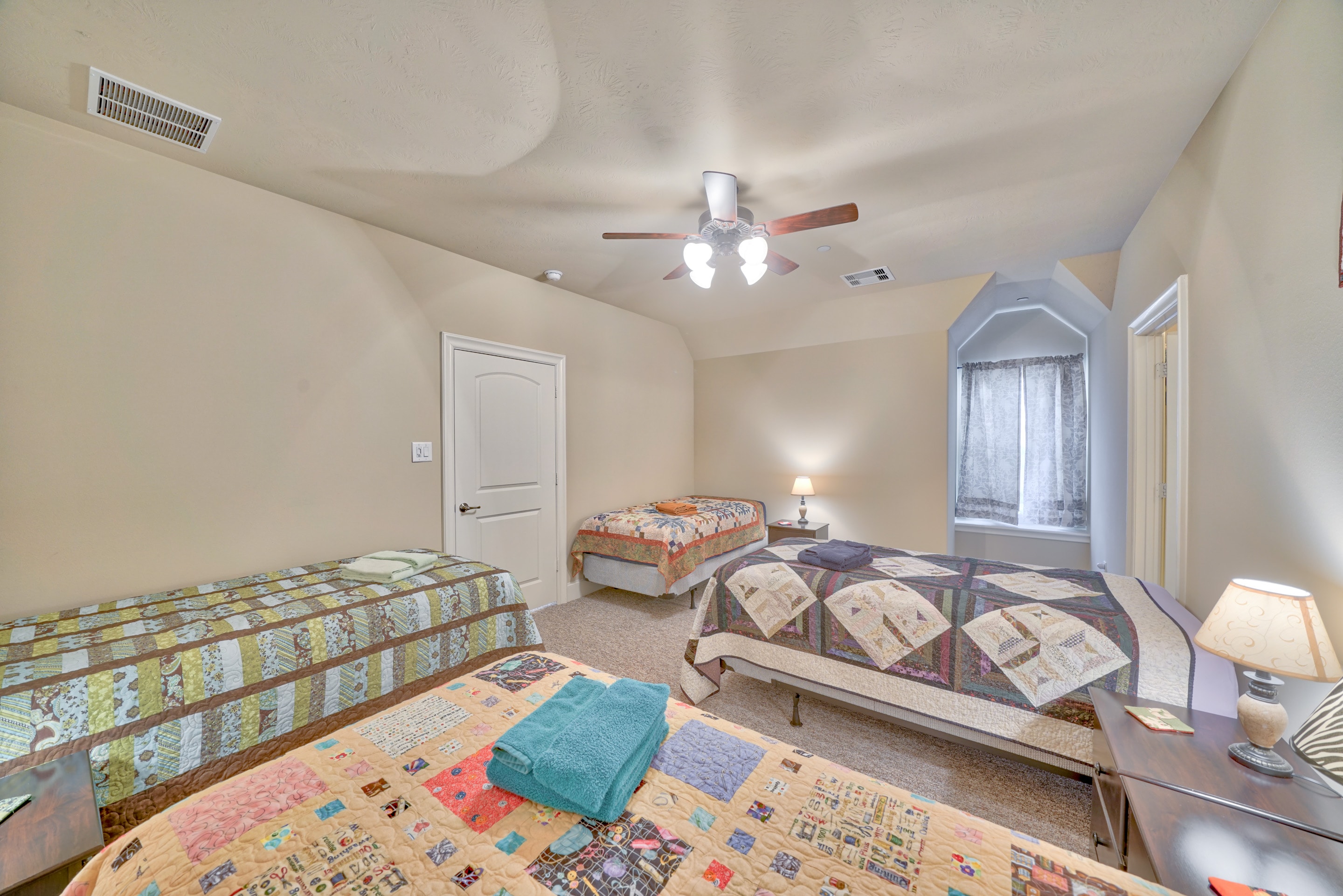 Large bedroom with three beds and colorful patchwork quilts