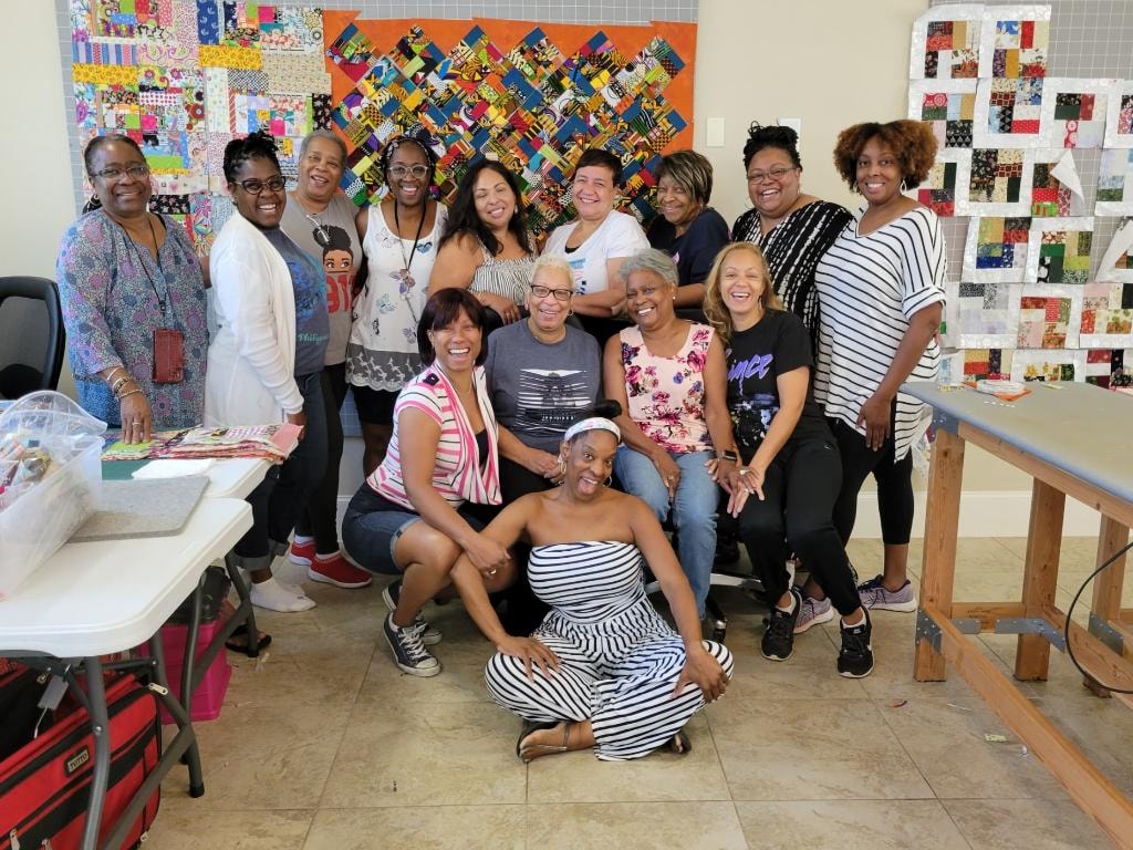 Vibrant group of quilters posing in front of colorful quilt blocks on the design walls