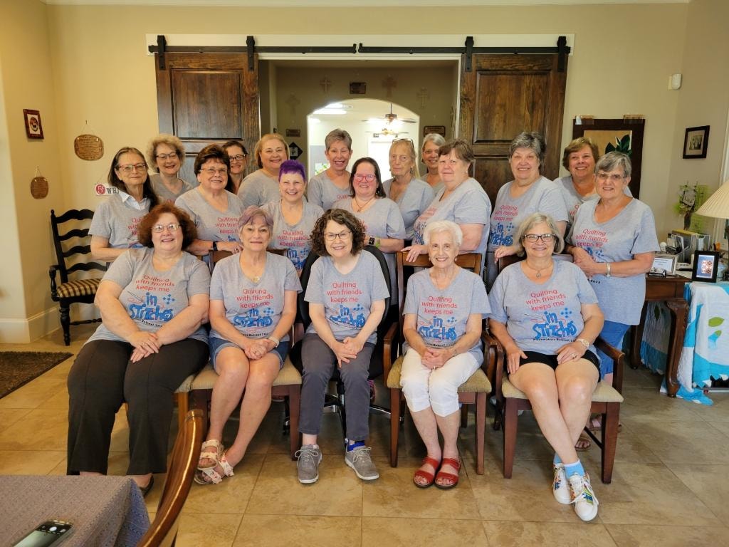 Large group of women in matching 'In Stitches' retreat t-shirts gathered in the sitting area
