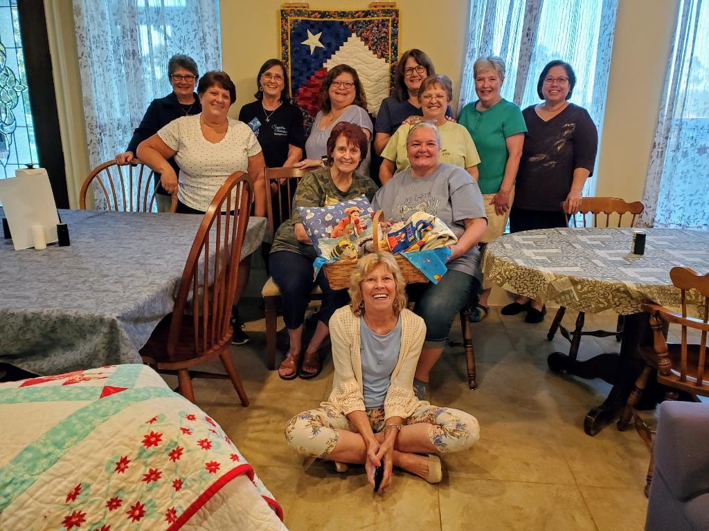 Group of women gathered in the dining area with quilts displayed during a retreat