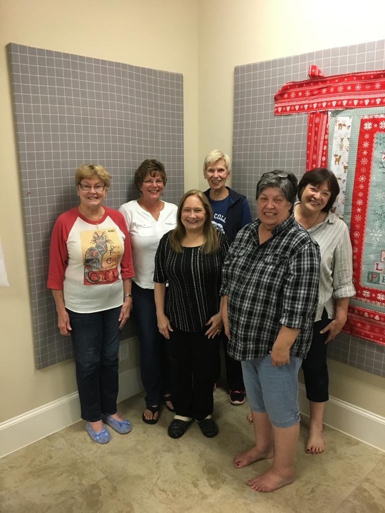 Group of six women posing in front of design walls with a Christmas quilt in progress
