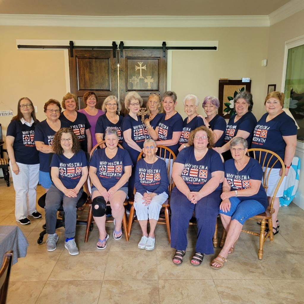 Large group of women in matching navy 'Sewciopath' retreat t-shirts in the sitting area