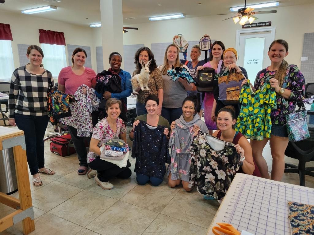 Group of women showing off completed sewing projects in the Magnolia Manor workroom