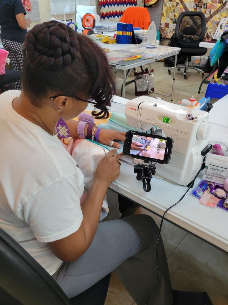 Guest sewing at a Janome machine while recording her work on a phone mounted to the machine