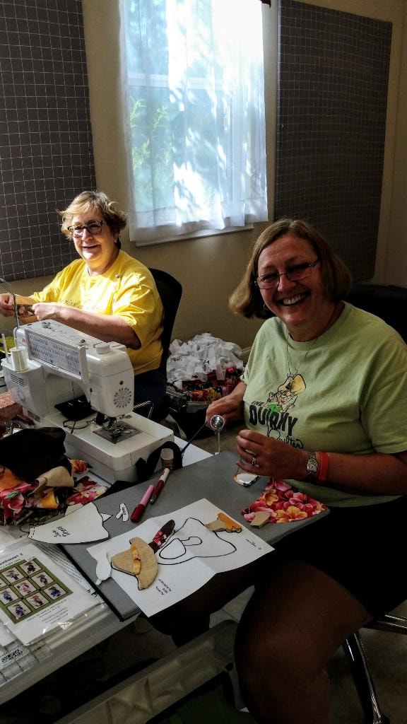 Two women laughing and sewing together at their machines in the Magnolia Manor workroom