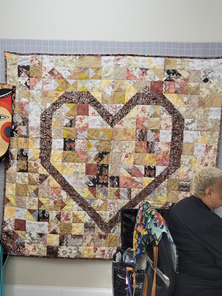 Patchwork quilt with a large heart design in brown, cream, yellow, and floral fabrics displayed on the design wall
