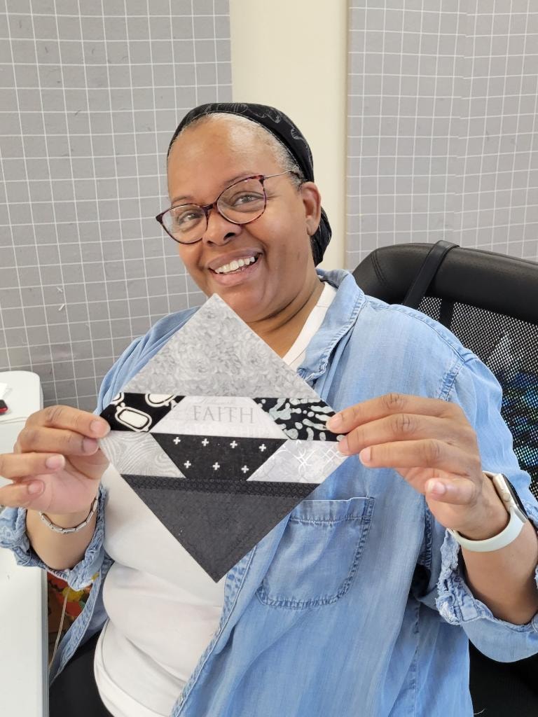 Quilter smiling and holding up a black and white Faith quilt block in the workroom