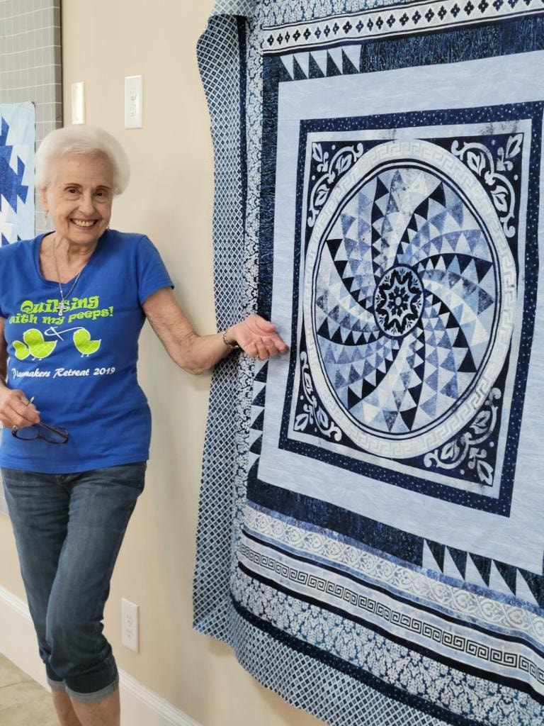 Quilter proudly displaying a stunning blue and white medallion quilt on the design wall