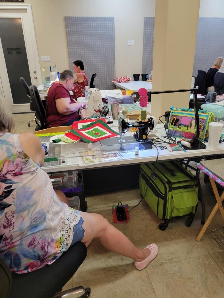 Quilters working at sewing machines with projects spread across the workroom tables